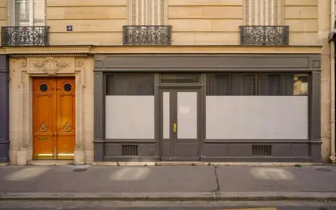 Une porte de commerce grise et une porte d'entrée en bois ornent cette façade parisienne.