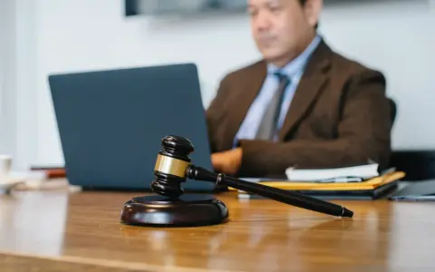 Marteau de juge sur un bureau, avec un homme en costume travaillant sur un ordinateur portable en arrière-plan. Explication de l'article 1722 du Code civil.