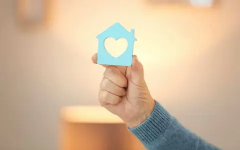 Main d'une personne tenant une maison bleue avec un cœur, symbole d'un projet de reprise de bail logement social.