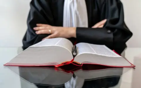 Un avocat en robe noire, penché sur un gros livre ouvert, symbolise la **notoriété acquisitive** par la maîtrise du droit.