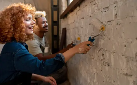 Un couple peint un mur en brique, résolvant un désaccord sur les travaux en indivision avec bonne humeur.