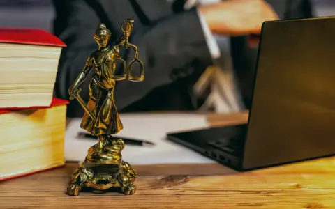 Statue de la justice, livres, ordinateur portable et stylo sur un bureau en bois. Un avocat examine les frais de donation.
