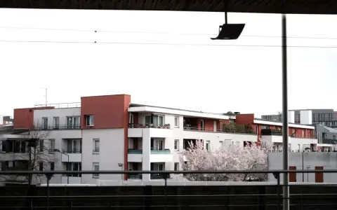Immeubles modernes avec balcons fleuris, évoquant un **logement décent loi 1989**. Un cerisier en fleurs ajoute une touche printanière.