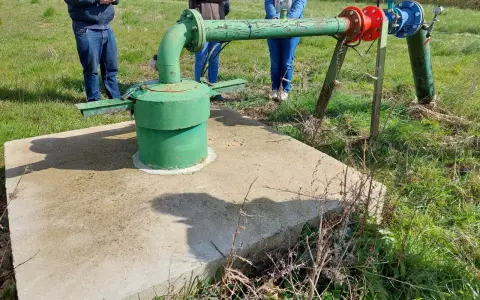 Installation de forage agricole, respectant la réglementation. Des personnes observent le système de pompage et de tuyauterie verte et bleue.