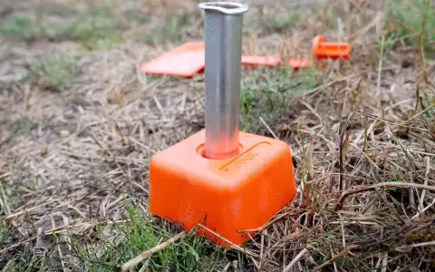 Borne orange avec un tube métallique planté dans le sol. D'autres bornes sont visibles en arrière-plan, indiquant le bornage d'un terrain déjà borné.