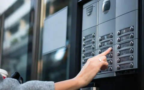 Une main appuie sur un bouton d'interphone, rappelant l'obligation du propriétaire d'assurer ce système.