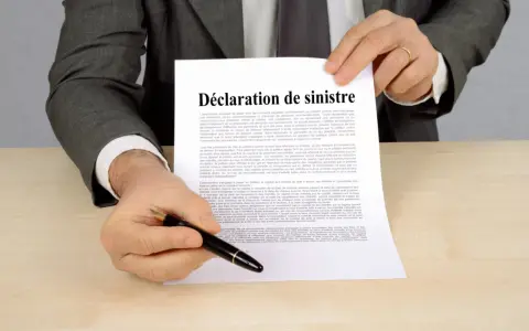 Un homme en costume gris tient un document intitulé "Déclaration de sinistre", prêt à signer.