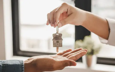 Une main tend une clé avec un pendentif en forme de maison, symbolisant une convention d'occupation anticipée avant vente.