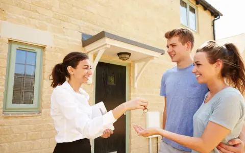 Une femme remet des clés à un jeune couple devant leur nouvelle maison. Le tableau droit de préemption locataire est respecté.