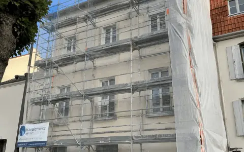Ravalement de façade en cours, échafaudages recouvrant le bâtiment. Une bâche blanche protège une partie des travaux. L'indemnisation locataire est une préoccupation lors de ces rénovations.