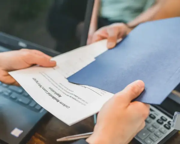 Des mains échangent des documents, un formulaire de prêt hypothécaire. La gestion de la durée de conservation des actes notariés est essentielle.