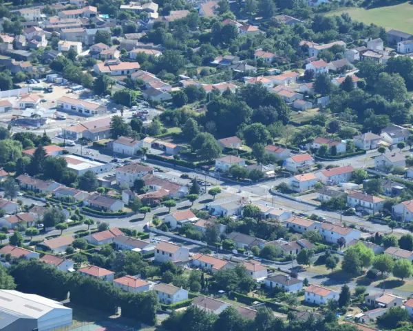 Vue aérienne d'un quartier résidentiel verdoyant, avec des maisons aux toits de tuiles rouges et des rues sinueuses. On aperçoit des chantiers, signe de développement, peut-être pour un nouveau plu à Niort.