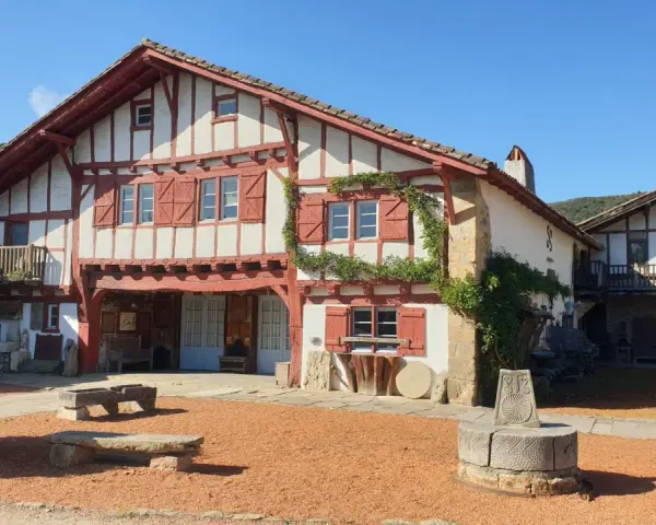 Maison basque traditionnelle à colombages rouges et blancs, avec un puits ancien devant. Un lieu plein de charme à Saint-Pée-sur-Nivelle.