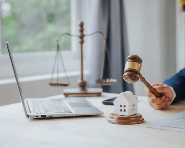 Marteau de juge frappant une maison miniature, symbolisant la loi Carrez pour une maison individuelle. Balance de la justice et ordinateur en arrière-plan.
