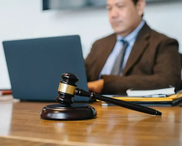 Marteau de juge sur un bureau, avec un homme en costume travaillant sur un ordinateur portable en arrière-plan. Explication de l'article 1722 du Code civil.