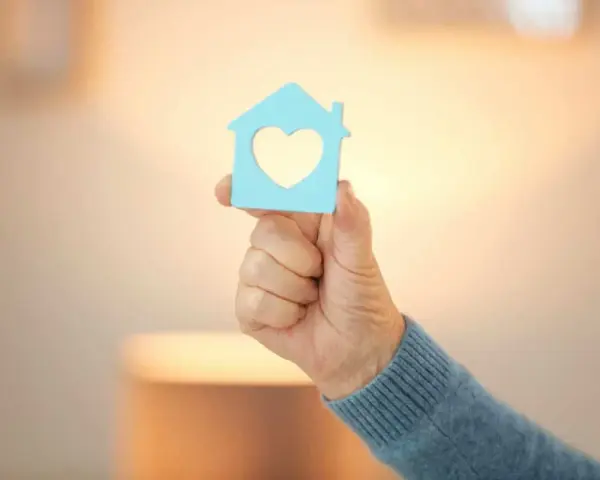 Main d'une personne tenant une maison bleue avec un cœur, symbole d'un projet de reprise de bail logement social.