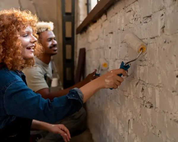 Un couple peint un mur en brique, résolvant un désaccord sur les travaux en indivision avec bonne humeur.