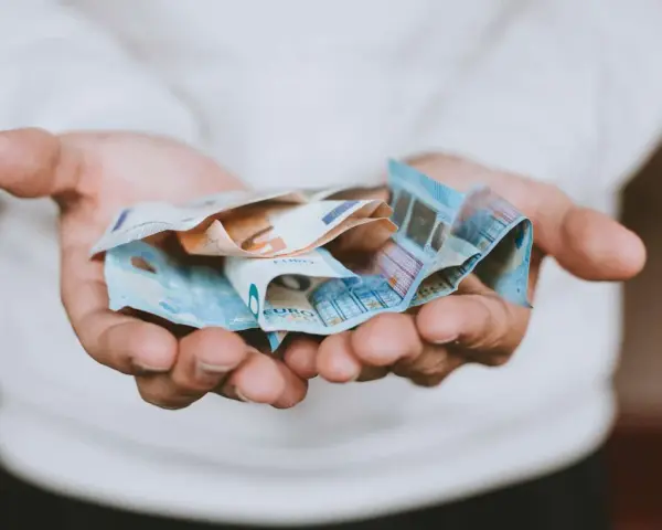 Mains tenant des billets en euros froissés, évoquant une transaction financière, peut-être une donation déguisée ou un viager.