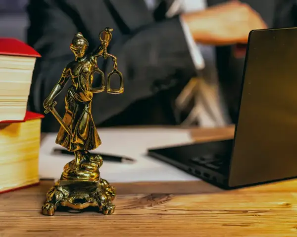 Statue de la justice, livres, ordinateur portable et stylo sur un bureau en bois. Un avocat examine les frais de donation.