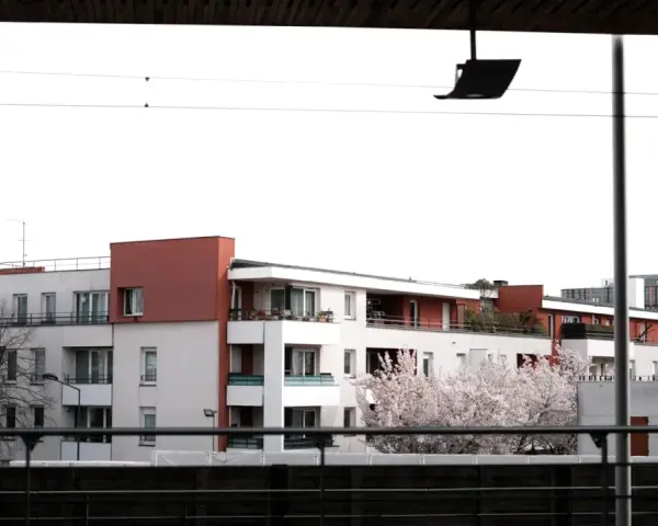Immeubles modernes avec balcons fleuris, évoquant un **logement décent loi 1989**. Un cerisier en fleurs ajoute une touche printanière.