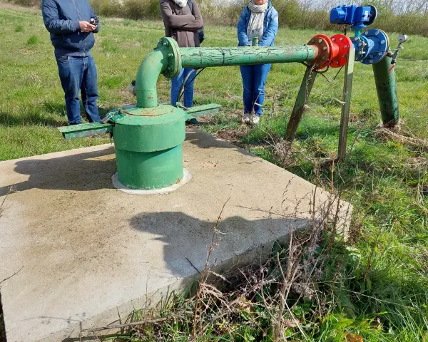 Installation de forage agricole, respectant la réglementation. Des personnes observent le système de pompage et de tuyauterie verte et bleue.