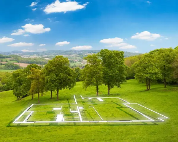 Plan d'une maison superposé sur un terrain verdoyant, illustrant la constructibilité d'un terrain. Paysage bucolique sous un ciel bleu.