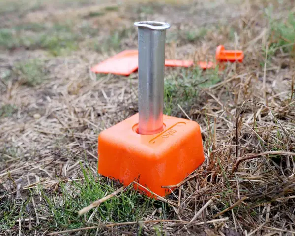 Borne orange avec un tube métallique planté dans le sol. D'autres bornes sont visibles en arrière-plan, indiquant le bornage d'un terrain déjà borné.