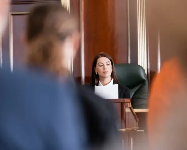 Une avocate présente son dossier, le dol, devant un juge. La salle d'audience est sombre et solennelle.