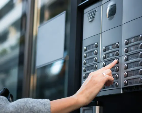 Une main appuie sur un bouton d'interphone, rappelant l'obligation du propriétaire d'assurer ce système.
