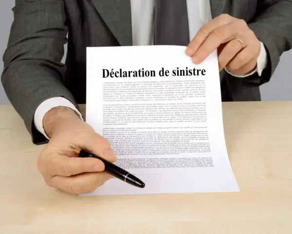 Un homme en costume gris tient un document intitulé "Déclaration de sinistre", prêt à signer.