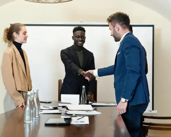Trois personnes en tenue d'affaires se serrent la main. L'un d'eux discute des intérêts d'un compte séquestre notaire.