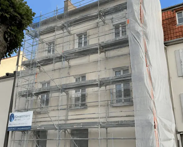Ravalement de façade en cours, échafaudages recouvrant le bâtiment. Une bâche blanche protège une partie des travaux. L'indemnisation locataire est une préoccupation lors de ces rénovations.