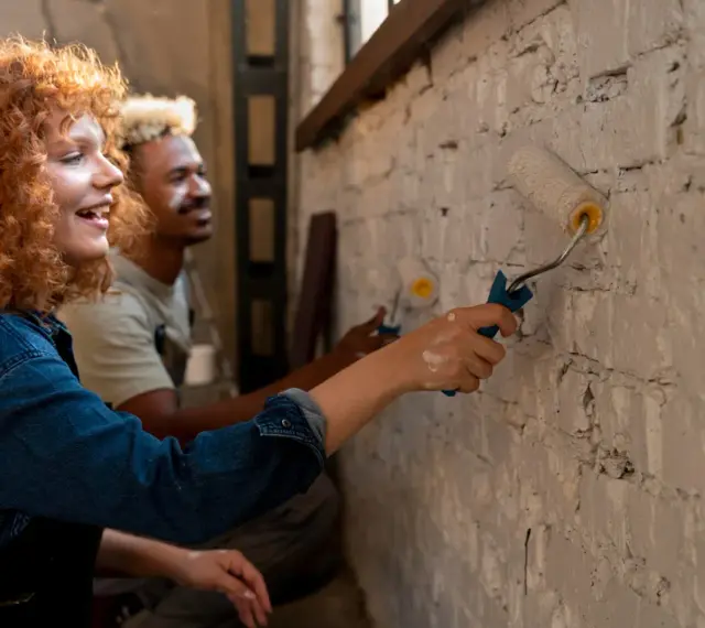 Un couple peint un mur en brique, résolvant un désaccord sur les travaux en indivision avec bonne humeur.