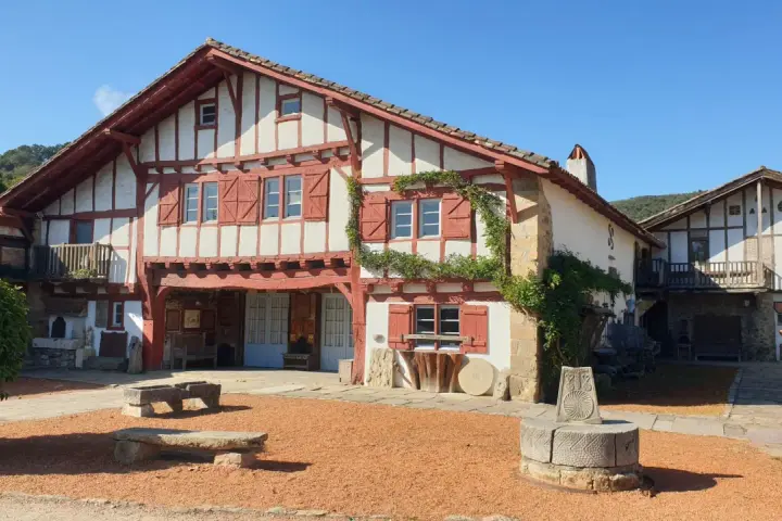 Maison basque traditionnelle à colombages rouges et blancs, avec un puits ancien devant. Un lieu plein de charme à Saint-Pée-sur-Nivelle.