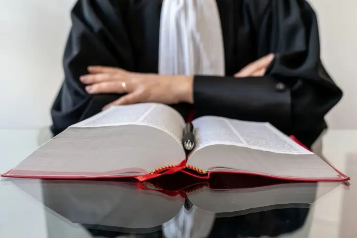 Un avocat en robe noire, penché sur un gros livre ouvert, symbolise la **notoriété acquisitive** par la maîtrise du droit.