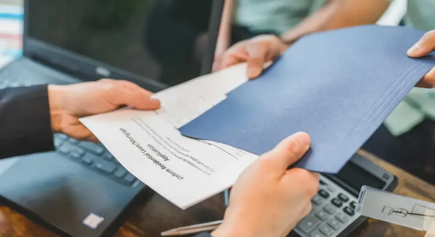 Des mains échangent des documents, un formulaire de prêt hypothécaire. La gestion de la durée de conservation des actes notariés est essentielle.