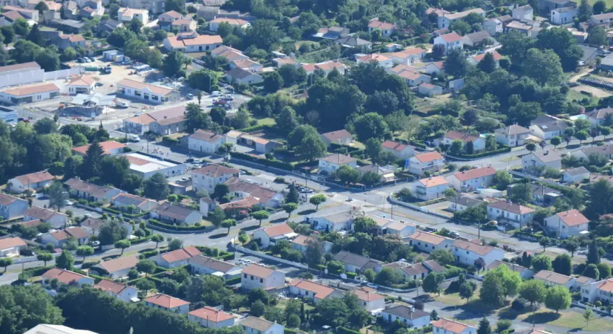 Vue aérienne d'un quartier résidentiel verdoyant, avec des maisons aux toits de tuiles rouges et des rues sinueuses. On aperçoit des chantiers, signe de développement, peut-être pour un nouveau plu à Niort.