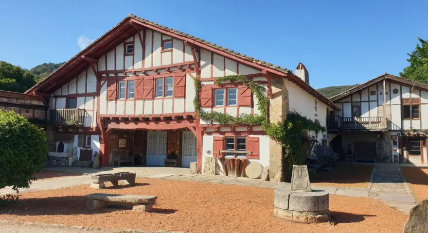 Maison basque traditionnelle à colombages rouges et blancs, avec un puits ancien devant. Un lieu plein de charme à Saint-Pée-sur-Nivelle.