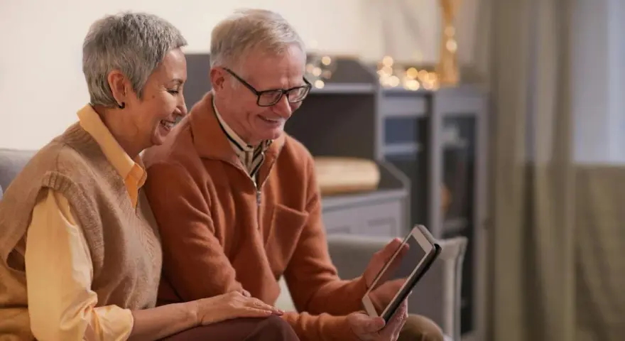 Un couple âgé regarde une tablette, peut-on louer un appartement après 70 ans ? Ils semblent heureux de leurs recherches.
