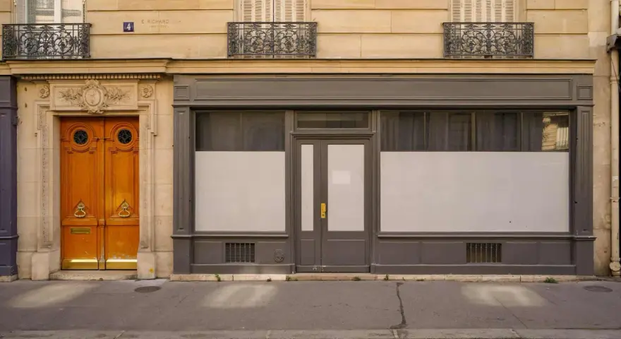 Une porte de commerce grise et une porte d'entrée en bois ornent cette façade parisienne.