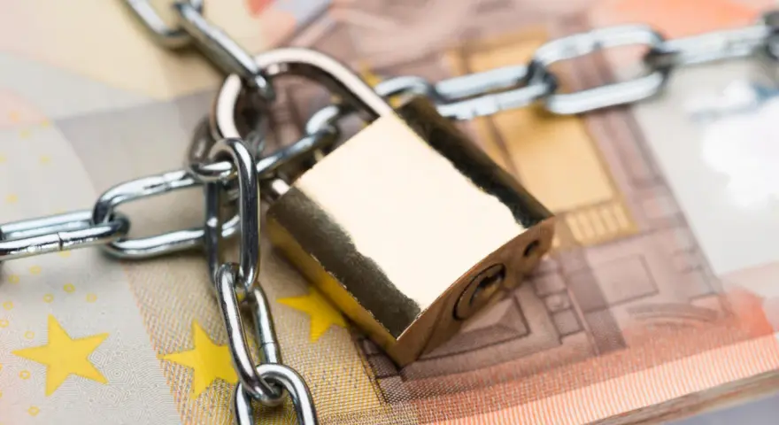 Un cadenas et une chaîne sécurisent des billets en euros, symbolisant la consignation de loyer ou la protection de fonds.