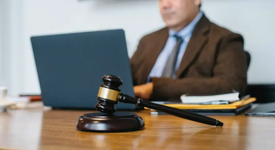Marteau de juge sur un bureau, avec un homme en costume travaillant sur un ordinateur portable en arrière-plan. Explication de l'article 1722 du Code civil.