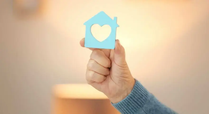 Main d'une personne tenant une maison bleue avec un cœur, symbole d'un projet de reprise de bail logement social.