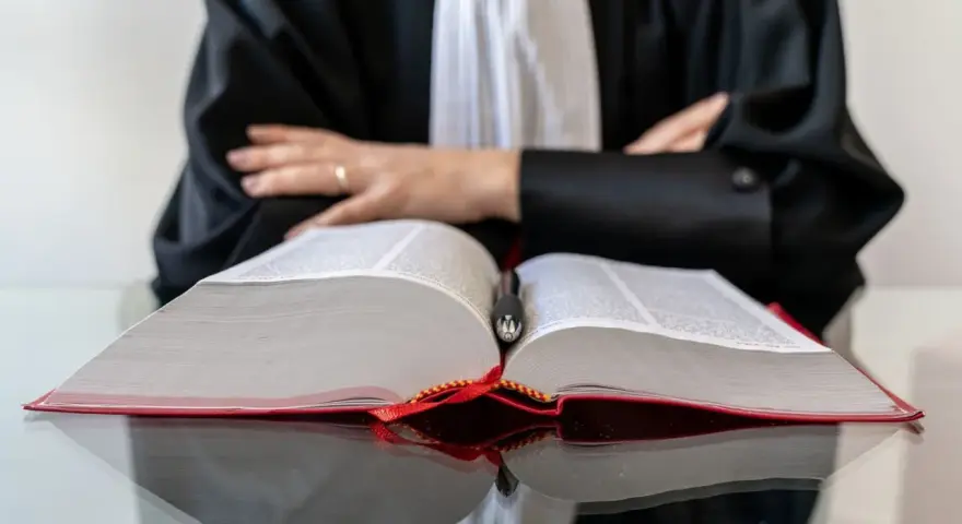 Un avocat en robe noire, penché sur un gros livre ouvert, symbolise la **notoriété acquisitive** par la maîtrise du droit.