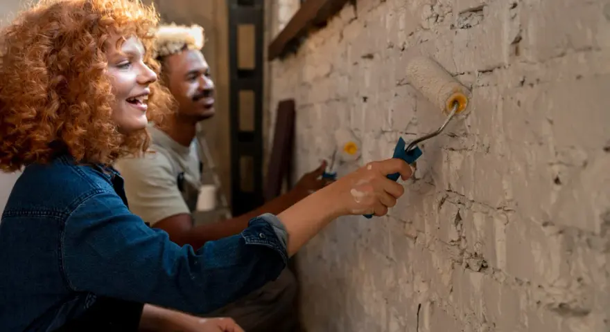 Un couple peint un mur en brique, résolvant un désaccord sur les travaux en indivision avec bonne humeur.