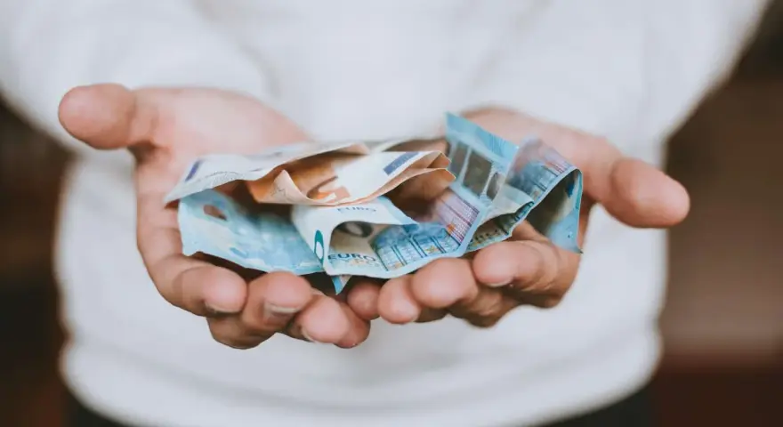 Mains tenant des billets en euros froissés, évoquant une transaction financière, peut-être une donation déguisée ou un viager.