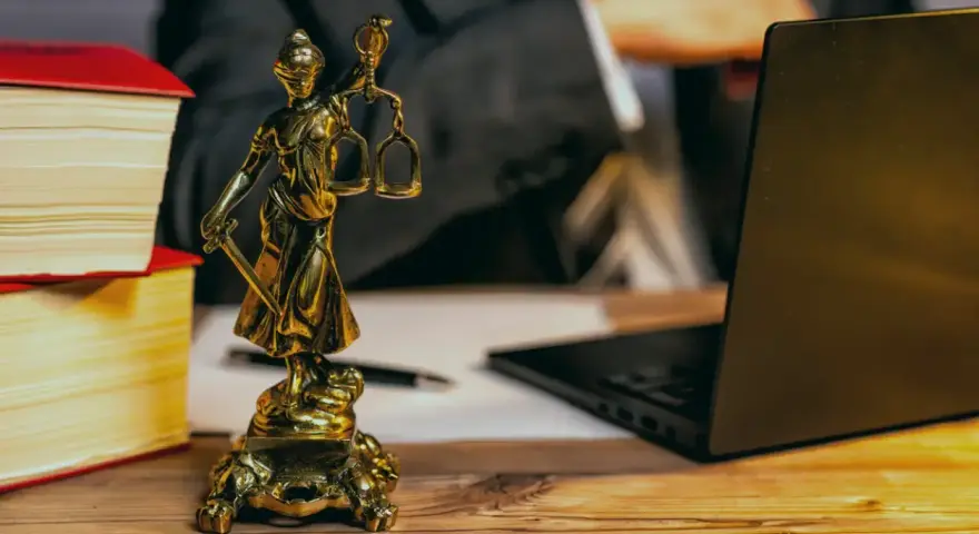 Statue de la justice, livres, ordinateur portable et stylo sur un bureau en bois. Un avocat examine les frais de donation.