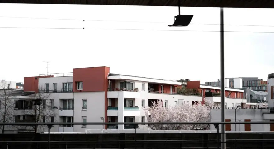 Immeubles modernes avec balcons fleuris, évoquant un **logement décent loi 1989**. Un cerisier en fleurs ajoute une touche printanière.