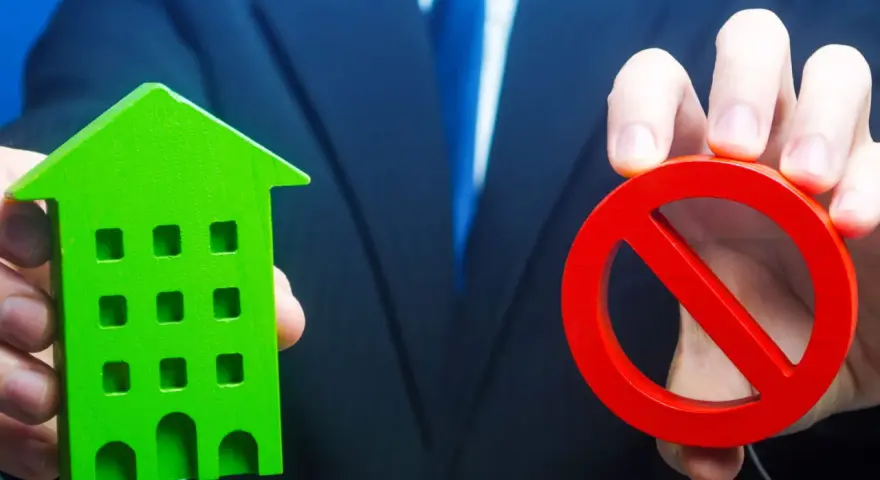 Un homme en costume tient une maison verte et un panneau d'interdiction rouge, symbolisant l'opposition au prix de vente chez le notaire.
