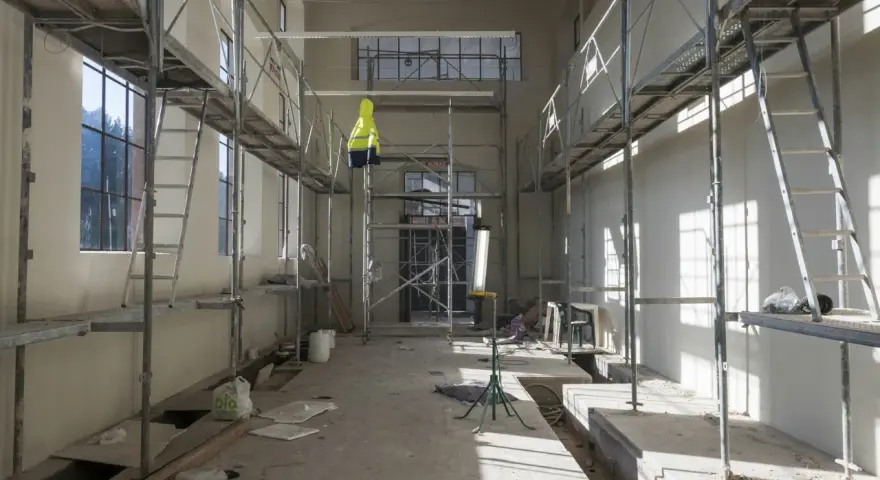 Chantier intérieur avec échafaudages, un gilet jaune suspendu, des matériaux de construction et des ouvertures. Un **daact non conforme** pourrait être la raison de cette scène.